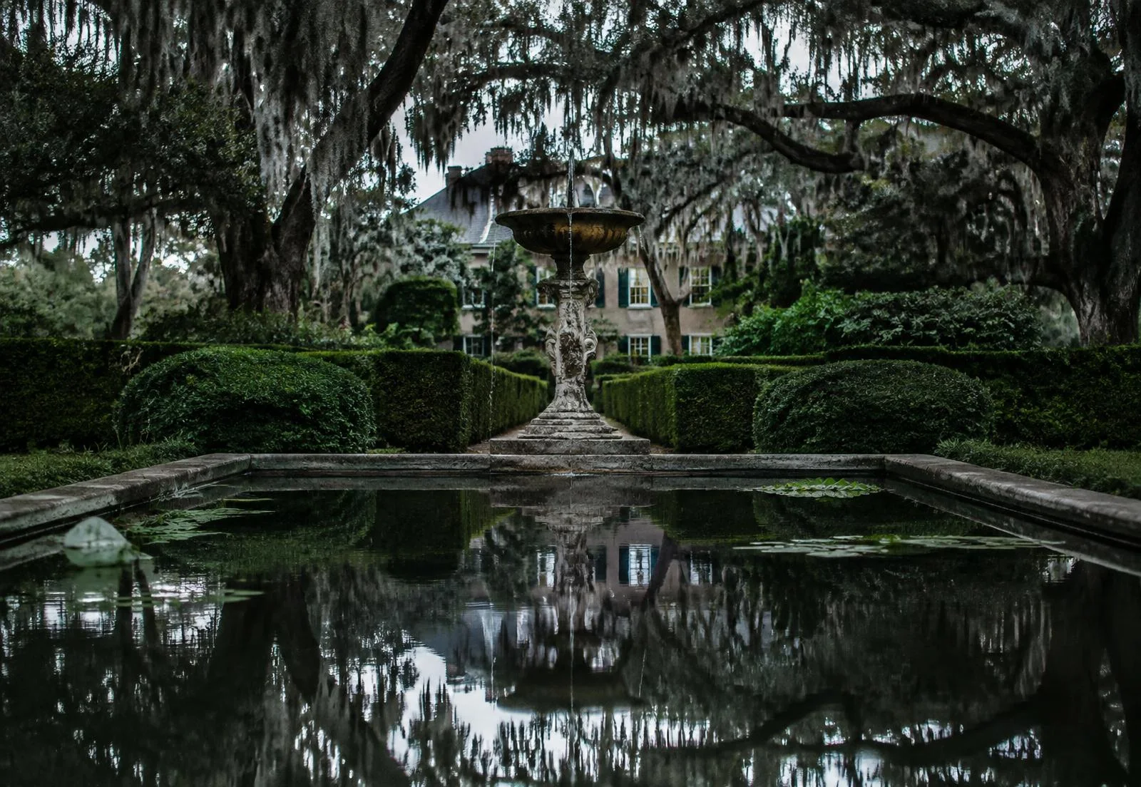 Stone fountain and reflecting pool beneath moss-draped oaks